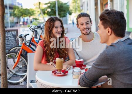 -MODELL VERÖFFENTLICHT. Drei jungen Freunden im Café mit heißen Getränken, lächelnd. Stockfoto