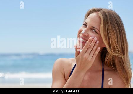 -MODELL VERÖFFENTLICHT. Junge Frau, die Anwendung von Sonnencreme am Strand. Stockfoto