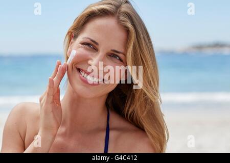 -MODELL VERÖFFENTLICHT. Junge Frau, die Anwendung von Sonnencreme auf ihre Wange. Stockfoto