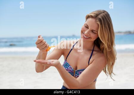 -MODELL VERÖFFENTLICHT. Junge Frau, die Anwendung von Sonnencreme am Strand. Stockfoto