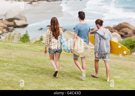 -MODELL VERÖFFENTLICHT. Drei junge Erwachsene, die zu Fuß in Richtung Strand mit Surfbrettern. Stockfoto