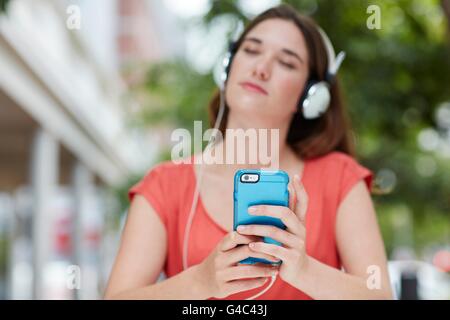 -MODELL VERÖFFENTLICHT. Junge Frau mit Kopfhörern anhören von Musik auf Smartphone. Stockfoto