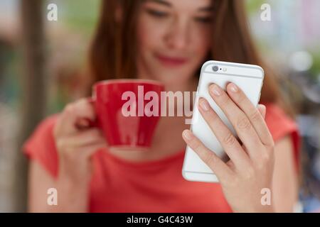 -MODELL VERÖFFENTLICHT. Junge Frau mit Smartphone, Kaffee trinken, Nahaufnahme. Stockfoto