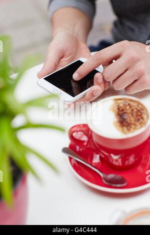 -MODELL VERÖFFENTLICHT. Person mit Smartphone mit Kaffee, Nahaufnahme. Stockfoto