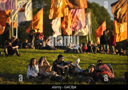 Nachtschwärmer entspannen sich und beobachten den Sonnenuntergang, während der Tag zu Ende geht und die Menschen sich auf die Abendfeiern beim Glastonbury Festival vorbereiten. Stockfoto