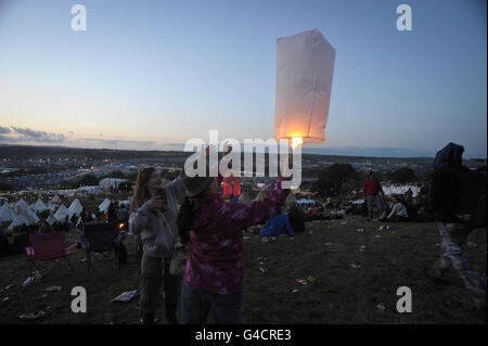 Nachtschwärmer beleuchten Laternen während des Sonnenuntergangs in der Nähe des Parkbereichs beim Glastonbury Musikfestival auf der Worthy Farm, Pilton. Stockfoto