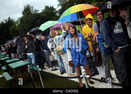 Tennisspieler schützen sich vor Regen, während sie am fünften Tag der Wimbledon Championships 2011 im All England Lawn Tennis Club, Wimbledon, Schlange stehen, um Tickets zu verkaufen. Stockfoto