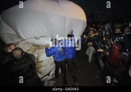 Sicherheitspersonal und Mitglieder der direkten Aktionsgruppe Art Uncut, tossle über einen 20 Fuß großen Ballon mit der Botschaft "U Pay Your Tax 2", während die Rockband U2 auf der Pyramid Stage beim Glastonbury Musikfestival in Worthy Farm, Pilton auftreten. Stockfoto