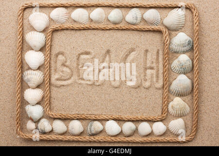 Schöner Rahmen von Seil und Muscheln im Sand mit Inschrift Strand als Hintergrund Stockfoto