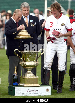 Der Duke of Edinburgh (links) überreicht dem englischen Kapitän Luke Tomlinson (rechts) beim Cartier International Polo Event im Guards Polo in Windsor, Berkshire, die 100. Krönungs-Cup-Trophäe an das siegreiche Team England. Stockfoto