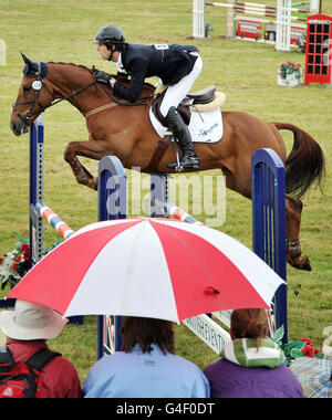 Die Menge beobachtet unter Regenschirmen, wie Clarke Johnstone beim Springreiten von Incognito III beim Festival of British Eventing im Gatcombe Park, Gloucestershire, zuschaut. Stockfoto