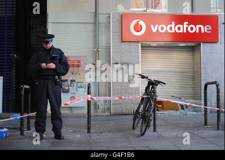 Ein Polizist steht vor einem Vodafone-Geschäft in Brixton, im Süden Londons, nach einer zweiten Nacht der Unruhen in der Hauptstadt. Stockfoto