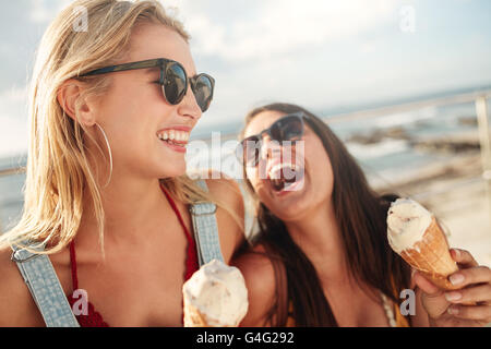 Zwei junge Frauen stehen, zusammen lachen und essen Eis. Glückliche junge Freundinnen mit Eis genießen gemeinsam auf eine Stockfoto