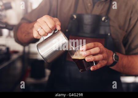 Beschnitten, Schuss Café Arbeiter Gießen Milch in eine Tasse Kaffee. Stockfoto