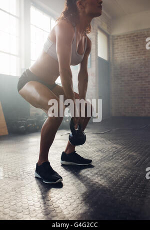 Sportliche Frau Training mit Wasserkocher Glocke während man in die Hocke. Muskulöse Frau Crossfit Training im Fitness-Studio zu tun. Stockfoto