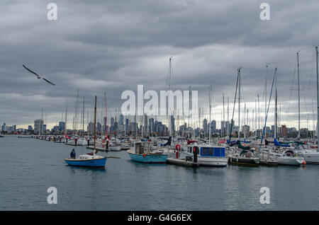 Ein Mann, der an einem bewölkten, bewölkten Tag mit einem kleinen Segelboot in einen Yachthafen in St. Kilda, Melbourne, Australien, fährt Stockfoto