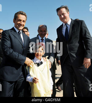 Premierminister David Cameron (rechts) und der französische Präsident Nicolas Sarkozy treffen auf dem Flughafen Benghazi lokale Kinder während eines eintägigen Besuchs in Libyen. Stockfoto