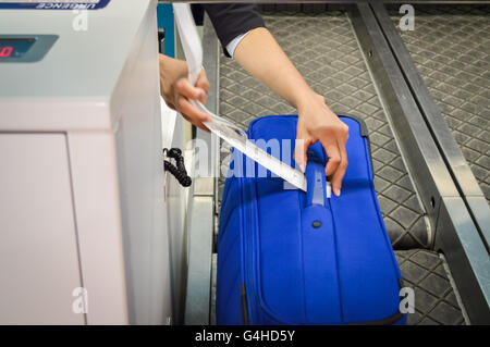 Check-in Mitarbeiter legt ein Gepäckanhänger Koffer von Passagier - Nahaufnahme von Händen Stockfoto