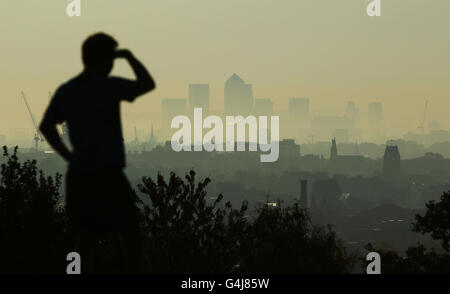 Ein Mann blickt vom Parliament Hill auf Hampstead Heath durch den frühen Morgennebel nach Canary Wharf, da sich die Hitzewelle in Teilen Großbritanniens bis in die nächste Woche fortsetzen wird, nach einem Wochenende rekordverdächtiger Temperaturen. Stockfoto