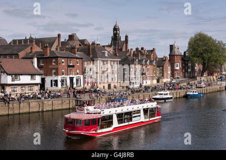 City Cruises Boot Segeln auf sonnigen malerischen Fluss Ouse an Menschen sitzen entspannt außerhalb Flussufer Pubs & Restaurants - York, Yorkshire, England, Großbritannien. Stockfoto