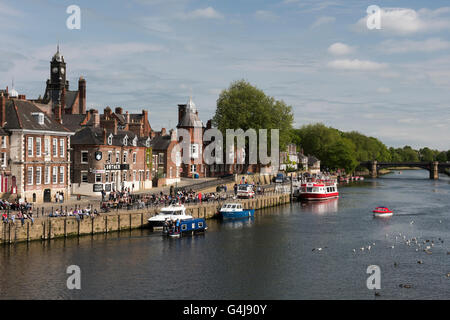 Viele Leute trinken und entspannen in der Sonne in einem geschäftigen Pub am Flussufer, während Freizeitboote auf dem Fluss Ouse fahren - King's Staith, York, North Yorkshire, England. Stockfoto