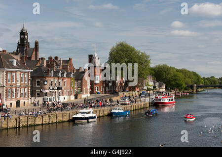 Viele Leute trinken und entspannen in der Sonne in einem geschäftigen Pub am Flussufer, während Freizeitboote auf dem Fluss Ouse fahren - King's Staith, York, North Yorkshire, England. Stockfoto