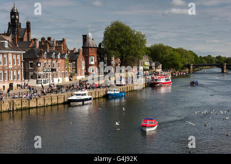 Viele Leute trinken und entspannen in der Sonne in einem geschäftigen Pub am Flussufer, während Freizeitboote auf dem Fluss Ouse fahren - King's Staith, York, North Yorkshire, England. Stockfoto