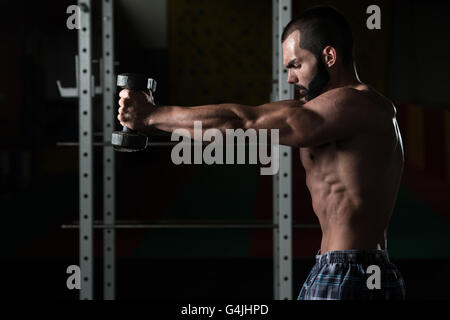 Junger Mann trainieren Schultern In einer dunklen Sporthalle - Bodybuilder schwere Übung für Schulter Stockfoto