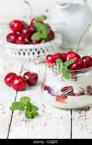 Sommer-Diät Frühstück. Joghurt mit frischen Kirschen Minze in einem Glas auf weißem Holz Hintergrund Stockfoto
