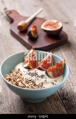 Frühstück mit Müsli, Joghurt, Feigen und Chia-Samen in einer blauen Schüssel auf einem hölzernen Hintergrund Stockfoto