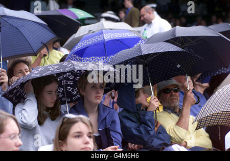 Keine kommerzielle Nutzung: Tennisfans auf dem Center Court decken sich unter dem Schirm, wenn der Regen während des Spiels von Tim Henman gegen Jim Courier bei den Wimbledon Tennis Championships aufhört zu spielen. Stockfoto