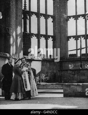 Königin Elizabeth II. Und der Herzog von Edinburgh mit dem Provost von Coventry, dem Very Rev. R.T Howard, im Sanctuary der alten Coventry Cathedral. Sie sehen das verkohlte Kreuz, das aus Balken auf dem Dach des Doms besteht, nachdem es in der Nacht vom 14. November 1940 von deutschen Bombern zerstört wurde. Stockfoto