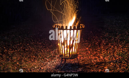 Nachtaufnahme von ein brennendes Feuer in einem Metallkorb mit Blätter auf dem Boden Stockfoto