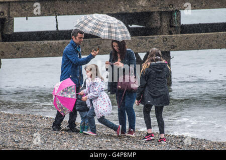 Aberystwyth, Wales, UK. 19. Juni 2016. UK-Wetter: Eine Familie bergende unter ihren Sonnenschirmen am Meer in Aberystwyth auf einem nassen und kalten Sonntagnachmittag Mitte Juni.    Als der längste Tag des Jahres - der Sommer-Sonnenwende - Ansätze, eine Bande von Starkregen fegt aus dem Westen, die meisten des Vereinigten Königreichs in den kommenden Tagen Credit ungewöhnlich kalte und bewölkte Bedingungen bringen: Keith Morris/Alamy Live-Nachrichten Stockfoto