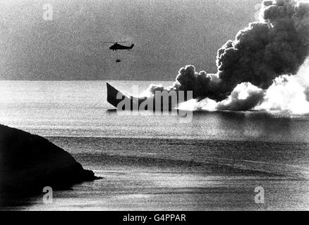 Ein Wessex-Hubschrauber schwebt über dem Wasser, während HMS Antelope, die immer noch heftig brennt, unter dem Wasser der Ajax Bay rutscht. Stockfoto