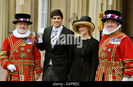 Der englische Cricketspieler Alastair Cook steht mit seiner Verlobten Alice Hunt und Mitgliedern der Leibgarde der Königin von Yeoman of the Guard, nachdem er von der Queen während einer Investiturzeremonie im Buckingham Palace, London, zu einem MBE gemacht wurde. Stockfoto