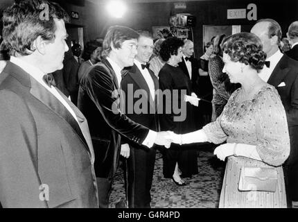 Queen Elizabeth II schüttelt sich die Hände mit dem Schauspieler Tom Courtenay, der von seinem Co-Star Albert Finney (im Vordergrund, links) bei der Royal Film Performance von 'The Dresser' in Odeon, Leicester Square, London, beobachtet wird Stockfoto