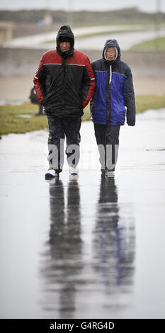 Menschen in feuchter Kleidung wandern an der Küste von Porthcawl, South Wales, entlang, während starke Winde und Regen den Südwesten Großbritanniens übertänsten. Stockfoto