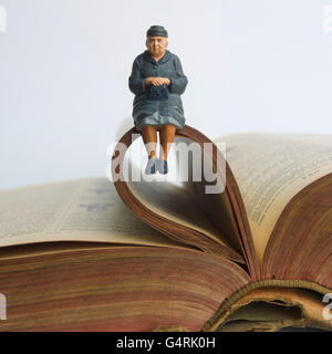 Ältere Dame, Miniatur Figur sitzt auf einem alten Buch Stockfoto