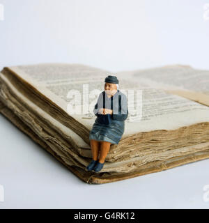 Ältere Dame, Miniatur Figur sitzt auf einem alten Buch Stockfoto