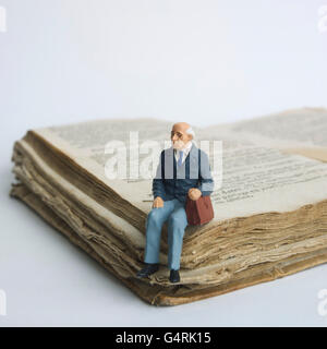 Älterer Mann, Miniatur Figur sitzt auf einem alten Buch Stockfoto