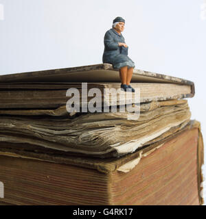 Ältere Dame, Miniatur Figur sitzt auf einem alten Buch Stockfoto