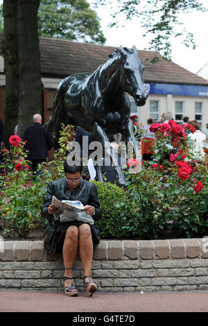 Pferderennen - Tag der Rose of Lancaster Stakes - Rennbahn Haydock Park. Ein Rennfahrer prüft die Form vor einer Statue eines Rennpferdes Stockfoto