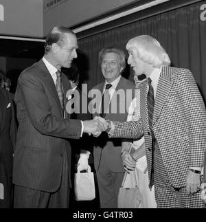 Ehrengast, der Herzog von Edinburgh, schüttelt sich die Hände mit der Persönlichkeit des Showbusiness Jimmy Savile (r), beobachtet von Sir Bernard Delfont (c), beim Mittagessen im Variety Club of Great Britain. Das Mittagessen stand neben dem National sponsored Walk des Variety Clubs, einem Teil der jährlichen Convention des Clubs International 1975. Stockfoto