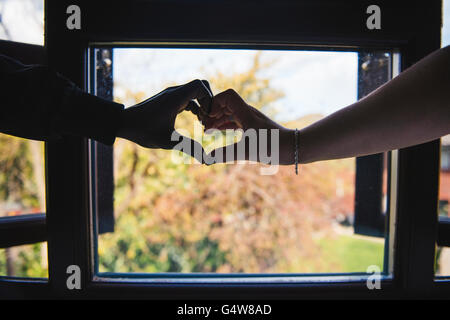 Herzförmige Hände gegen den Fensterhintergrund, Farbbild. Stockfoto