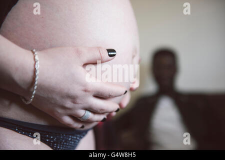 Eine Schwangerin hält ihren Babybauch. Der zukünftige Vater sitzt im Hintergrund; werdende Eltern. Stockfoto