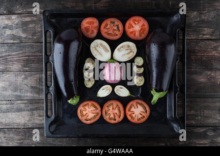 Ganze und geschnittene Auberginen und Tomaten auf rustikalen Backblech. Ansicht von oben. Stockfoto