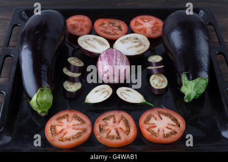 Ganze und geschnittene Auberginen und Tomaten auf rustikalen Backblech. Geringe Schärfentiefe Stockfoto