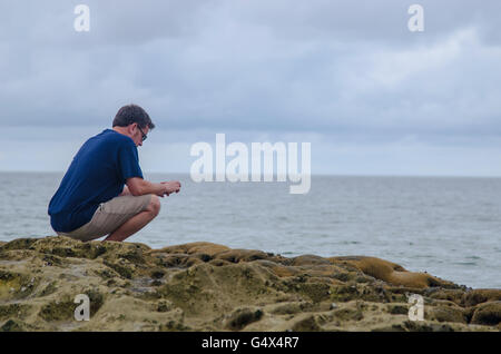 Horizontales Bild des sitzenden Menschen fotografieren am Strand gegen bewölktem Himmel in der Abenddämmerung Stockfoto