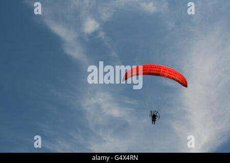 Niedrigen Winkel Ansicht der Person motor Paragliding mit rotem Schirm vor blauem Himmel mit Wolken Stockfoto